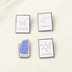 Puede incluir: Cuatro pines de esmalte con fondos blancos y bordes plateados. Tres pines presentan estructuras químicas con las palabras "SEROTONIN", "DOPAMINE" y "CAFFEINE". El cuarto pin representa una criatura morada en un vaso de precipitados con el número "6.022 x 10^23".