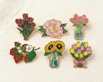 Könnte beinhalten: Set mit sechs floralen Emaille-Anstecknadeln. Designs umfassen Tulpen-, Sonnenblumen- und Pfingstrosensträuße sowie einen Erdbeerzweig. Jede Anstecknadel hat goldfarbenes Metall und leuchtende Farben, ideal, um jedem Outfit einen Hauch von Natur zu verleihen.