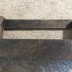 May include: A rectangular dark brown wooden crate with an open top and sides. The structure is composed of weathered, rough-hewn planks joined together with visible nails at the corners. The wood displays a natural grain and aged texture throughout.