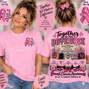 May include: A light pink t-shirt featuring a small breast cancer awareness ribbon on the front left chest. The back displays a graphic of five people standing before a building with the text Together We Make a Difference and Breast Cancer Awareness.