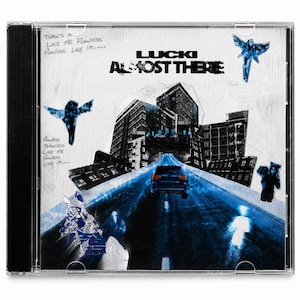 May include: A CD case featuring the album "Almost There" by Lucki. The cover art has a blue and white color scheme with a cityscape, a car on a road, and stylized figures. Text includes "LUCKI" and "ALMOST THERE."