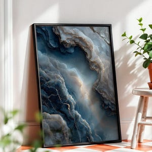 Op de afbeelding: Een ingelijste rechthoekige wandkunstprint met een abstract ontwerp van wervelende diepblauwe, grijze en witte tinten met subtiele gouden aders, die doet denken aan gelaagde steen, in een dunne zwarte lijst op een geblokte vloer.