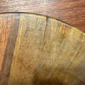 May include: A circular wooden board featuring a natural grain pattern with varying shades of brown, ranging from light tan to deep mahogany. A thin, vertical crack is visible near the curved edge of the board, extending toward the center.