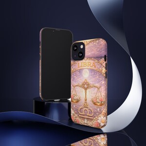 May include: A phone case featuring a Libra zodiac design. The case has a pink and gold color scheme with floral accents and the word "LIBRA" at the top. The design includes a scale, flowers, and a moon.