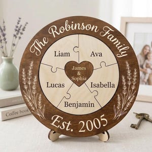 May include: A personalised wooden family puzzle with a dark brown frame and a light wood puzzle. The puzzle is engraved with the family name, individual names, and the year 2005. Decorative lavender sprigs are etched on the frame.