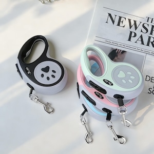 May include: Several retractable dog leads in pastel colours. One is black and white, the others are pink, blue, and green. Each lead has a paw print design and a metal clasp for attaching to a collar or harness.