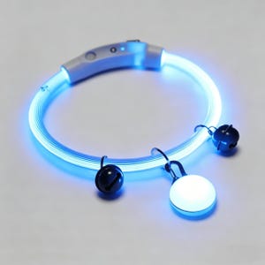 Puede incluir: Un collar azul brillante para mascotas con dos campanas negras y una luz blanca y redonda. El collar es un tubo circular con un panel de control gris claro. Las campanas y la luz están suspendidas del collar por pequeños ganchos de metal.