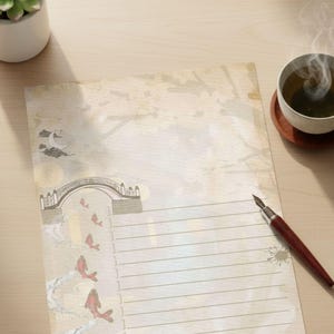 Puede incluir: Un juego de papelería con un papel rayado de estilo vintage con una ilustración de un puente y peces koi. Una pluma estilográfica y una taza de té humeante están sobre una superficie de madera. También hay una pequeña planta suculenta en una maceta blanca.