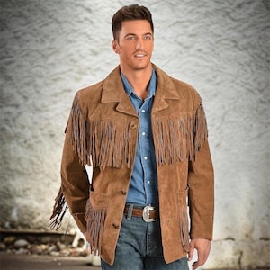 Könnte beinhalten: Braune Wildlederjacke mit Fransen. Die Jacke hat eine Knopfleiste, zwei Vordertaschen und einen Reverskragen. Das Model trägt ein blaues Jeanshemd und Jeans.