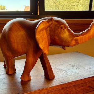 May include: A wooden elephant sculpture with a raised trunk, displaying detailed craftsmanship. The warm brown wood tones create a natural aesthetic. This decorative piece is a unique addition to any home. The sculpture is approximately 30 cm in length.
