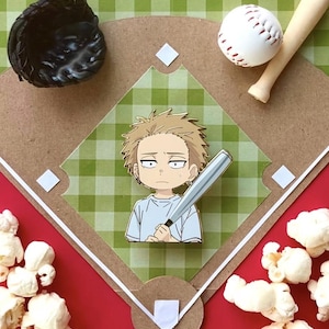 May include: A baseball-themed display featuring a baseball pin with a character holding a bat, a baseball, a bat, and a glove. The background includes a baseball diamond design, popcorn, and a red and green checkered pattern.