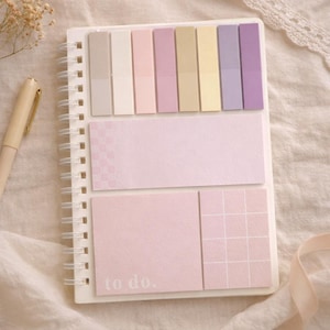 May include: A spiral-bound notebook featuring a collection of pastel-colored sticky notes in various shapes and sizes. The top section has eight vertical rectangular tabs, while the bottom includes a large rectangular note and a square grid note.