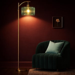 May include: A gold floor lamp with a green glass shade illuminates a dark red wall. A dark green velvet armchair with a light blue pillow sits nearby. A framed floral print hangs on the wall, creating a cozy, elegant atmosphere.