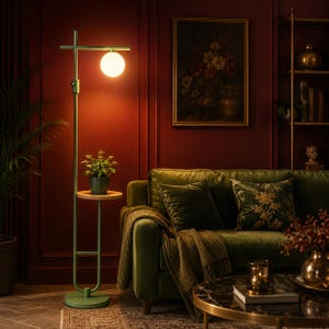 May include: A tall, matte green metal floor lamp featuring a circular wooden shelf and a single glowing spherical glass bulb at the top. The lamp has a slender, vertical frame with a round base and a horizontal arm extending to hold the light.