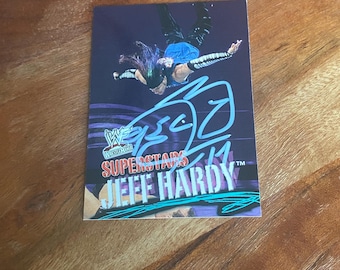 May include: A rectangular trading card featuring a photograph of Jeff Hardy in mid-air against a dark purple background. The card displays the WWF WrestleMania logo, the text SUPERSTARS, the name JEFF HARDY, and a prominent light blue autograph.