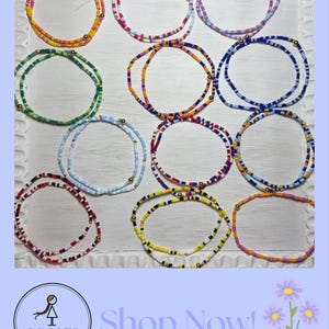 May include: A collection of colorful beaded waist beads in various designs. The beads are arranged in circles, showcasing a variety of colors including yellow, green, blue, red, and pink. The image includes the text "Shop Now!" and the "Ginger Girl" logo.