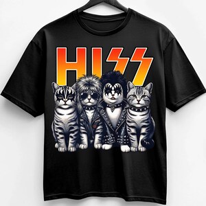 Pode incluir: Camiseta preta com um desenho de quatro gatos vestidos como a banda de rock KISS. A palavra "HISS" está impressa acima dos gatos em laranja e amarelo. Os gatos usam maquiagem e jaquetas de couro.