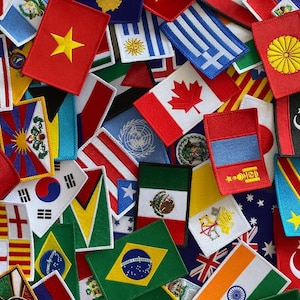 May include: A collection of embroidered flag patches, including the flags of the United States, Canada, Brazil, and Japan. The patches are rectangular and feature various colors and designs, showcasing national symbols.