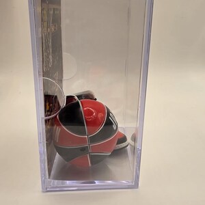 May include: A miniature basketball in a clear display case. The basketball is red, black, and white, with a segmented design. The case is rectangular and transparent, showcasing the collectible item.