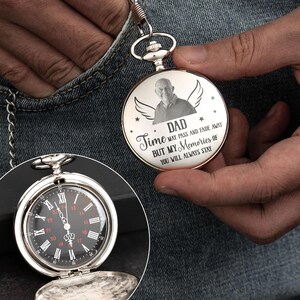 May include: Silver pocket watch with a black face and white Roman numerals. The watch has a chain and is open to reveal the time. The watch face has the text "DAD Time may pass and fade away but my memories of you will always stay."