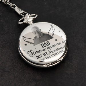 May include: A silver pocket watch with a chain. The watch face features a photo of a man, the word "DAD", angel wings, and the text "Time may pass and fade away but my memories of you will always stay."