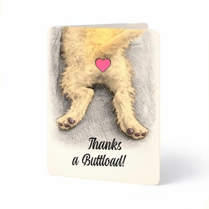 May include: A folded greeting card featuring a humorous illustration of a dog's rear end with a pink heart over it. The text "Thanks a Buttload!" is printed in black below the illustration.
