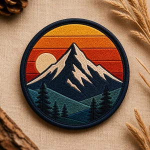 May include: Embroidered patch featuring a mountain scene with a sunset. The design includes a snow-capped mountain, a setting sun, and evergreen trees, all within a circular navy blue border. The color palette includes shades of orange, yellow, blue, and green.