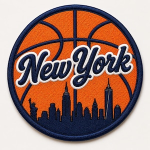 May include: A circular embroidered patch featuring an orange basketball design with dark blue lines. The text New York is written in a white and dark blue script font across the center. Below the text is a dark blue silhouette of the New York City skyline including the Statue of Liberty.