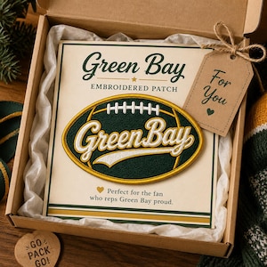 Puede incluir: Un parche bordado con las palabras "Green Bay" en forma de bal&oacute;n de f&uacute;tbol, y el texto "Green Bay EMBROIDERED PATCH" encima. Una etiqueta de regalo dice "For You". El parche est&aacute; en una caja de regalo.