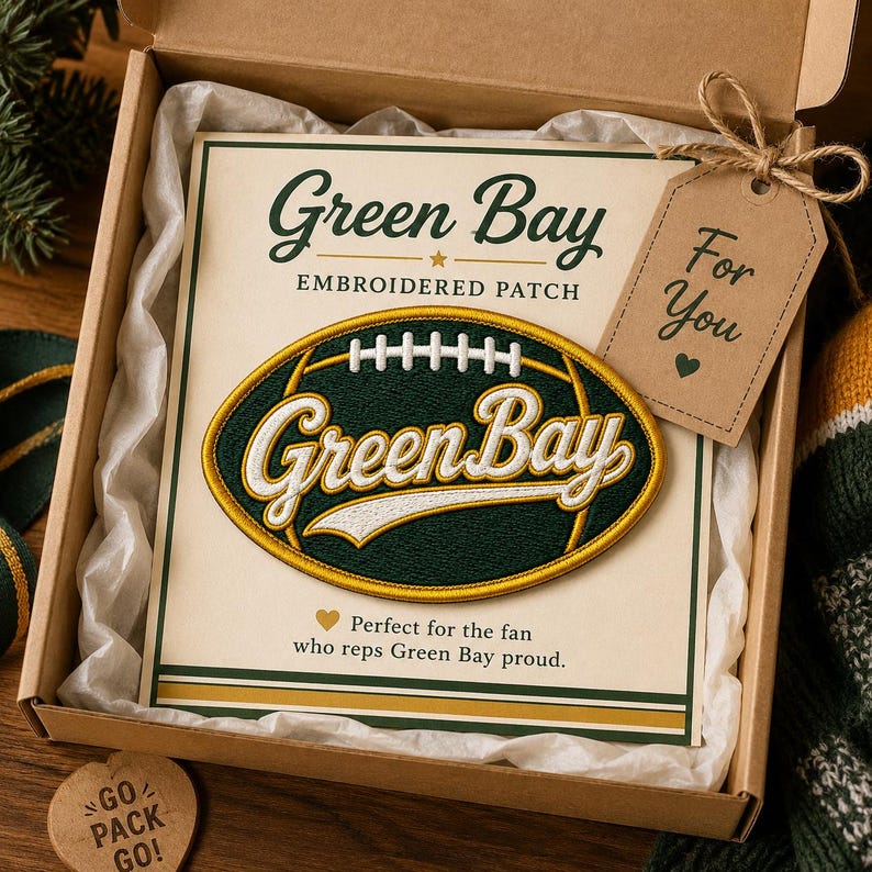 Puede incluir: Un parche bordado con las palabras "Green Bay" en forma de bal&oacute;n de f&uacute;tbol, y el texto "Green Bay EMBROIDERED PATCH" encima. Una etiqueta de regalo dice "For You". El parche est&aacute; en una caja de regalo.