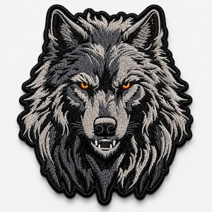 May include: An embroidered patch featuring the head of a wolf with detailed grey and black fur, sharp teeth, and piercing orange eyes. The design is outlined with a thick black border, showcasing intricate stitching that defines the facial features.