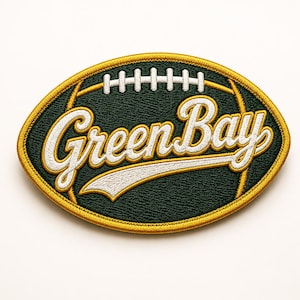May include: Embroidered patch in the shape of a football, featuring the words "Green Bay" in a stylized script. The patch has a dark green background with white and gold accents, and a gold border.