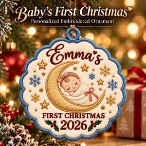 May include: A scalloped, cream-colored embroidered ornament with a blue border. It features a sleeping baby on a gold crescent moon, surrounded by gold stars and blue snowflakes. Text reads: Emma's FIRST CHRISTMAS 2026, with holly accents.