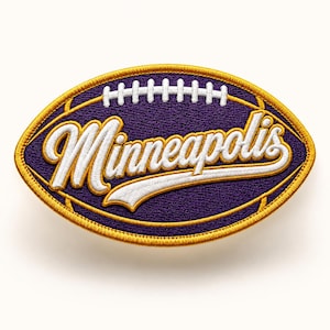 May include: Embroidered patch in the shape of a football, featuring the word "Minneapolis" in white script. The patch has a purple background with a gold border and white stitching.