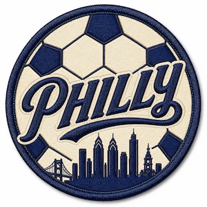 May include: A circular embroidered patch featuring a navy blue and cream soccer ball pattern. The word PHILLY is stitched in navy blue script across the center, with a navy blue silhouette of the Philadelphia city skyline below it.