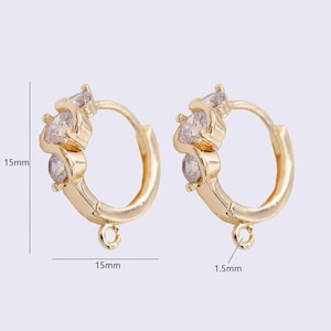 May include: A pair of gold-colored hoop earrings. Each earring features three clear, sparkling gemstones. The hoops are 15mm in diameter and have a small loop at the bottom. The earrings are a classic jewelry design.