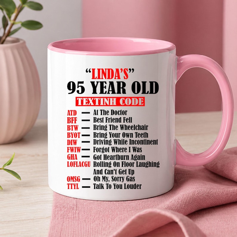 May include: White ceramic mug with a pink interior and handle. The mug features the text "LINDA'S" and "95 YEAR OLD TEXTINH CODE" in black, with a list of abbreviations and their meanings in red and black.