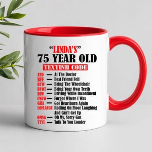 May include: A white ceramic mug with a red interior and handle. The mug features the text "LINDA'S" and "75 YEAR OLD" in black, with a list of acronyms and their meanings below. A humorous gift.