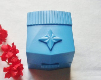 May include: A small, light blue ring box with a star design on the lid. The box is closed and sitting on a white surface.
