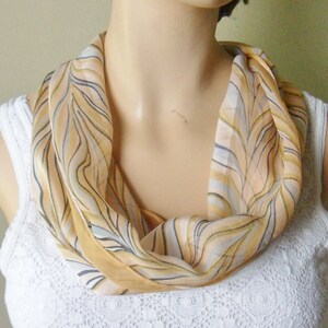 May include: A woman wearing a white lace top with a beige and brown patterned scarf around her neck.