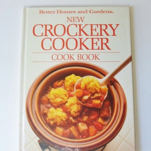 May include: A white cookbook with the title "New Crockery Cooker Cookbook" by Better Homes and Gardens. The cover features a close-up of a crock pot filled with a stew with dumplings.