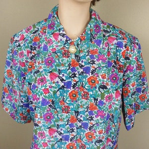 May include: A white short-sleeved button-down shirt with a colorful floral print. The print features red, orange, pink, purple, blue, and green flowers on a white background.