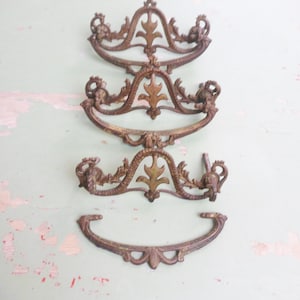 May include: Four antique bronze drawer pulls with ornate floral and scroll designs. The pulls vary in size and shape, with a weathered patina. These decorative hardware pieces are ideal for vintage furniture restoration projects.