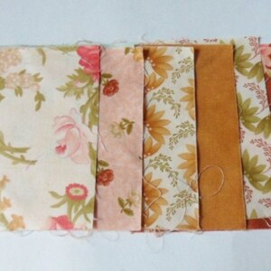 May include: A collection of fabric swatches in various floral patterns and solid colors. The fabrics include shades of cream, pink, orange, and brown. The floral patterns feature roses and other botanical designs, suitable for quilting or crafting projects.