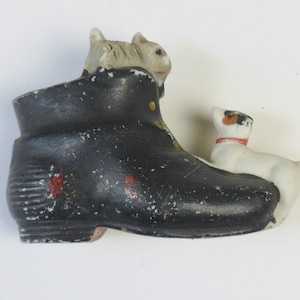 May include: A black ceramic boot with a white cat figurine sitting on top and a white dog figurine sitting on the side of the boot.