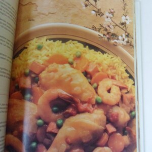 May include: A close-up of a bowl of paella, a Spanish rice dish, with chicken, shrimp, peas, and carrots. The paella is served with a side of yellow rice.