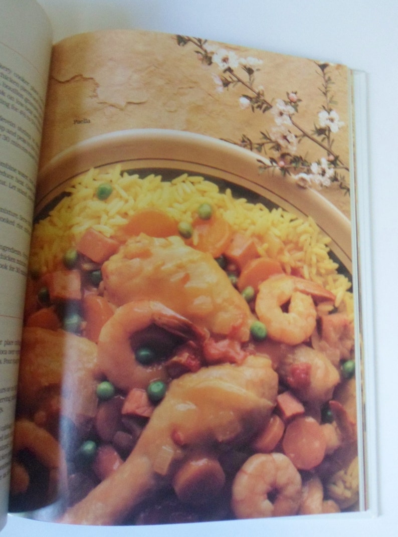 May include: A close-up of a bowl of paella, a Spanish rice dish, with chicken, shrimp, peas, and carrots. The paella is served with a side of yellow rice.