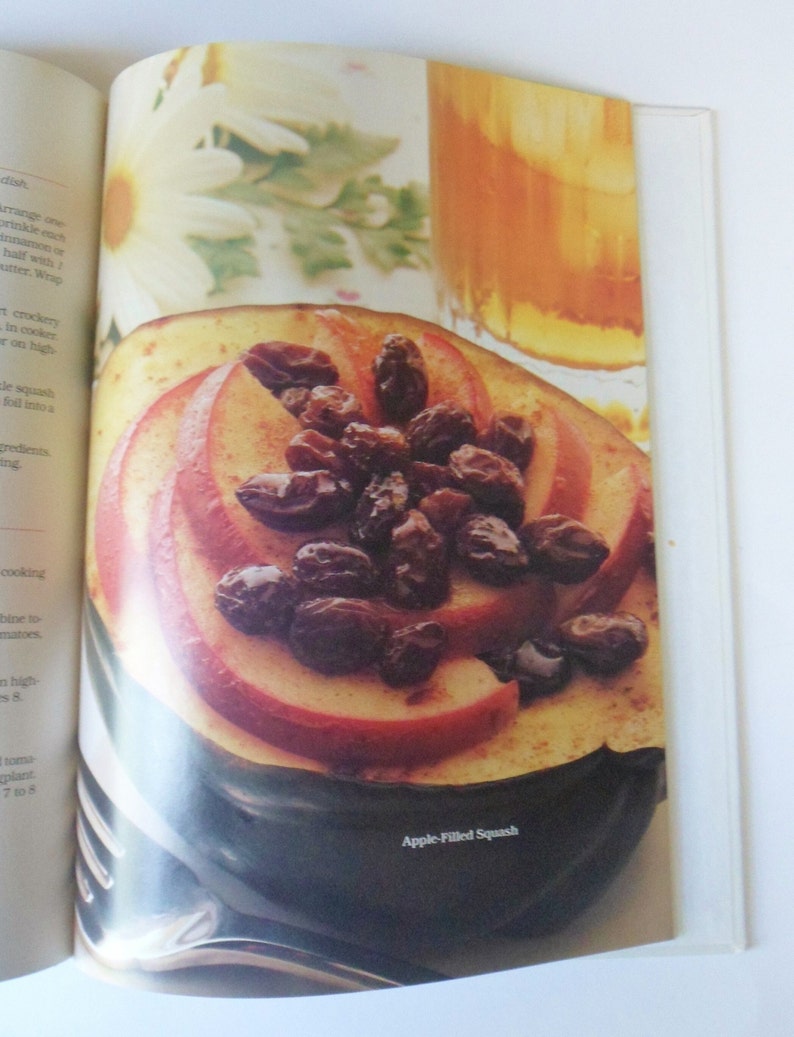 May include: A close-up of a halved acorn squash filled with sliced apples and raisins. The squash is on a dark brown surface and the text "Apple-Filled Squash" is printed below it.