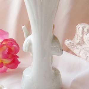 May include: White porcelain vase with a floral design. The vase is shaped like a trumpet and has a flared opening. The floral design is in shades of pink and yellow.