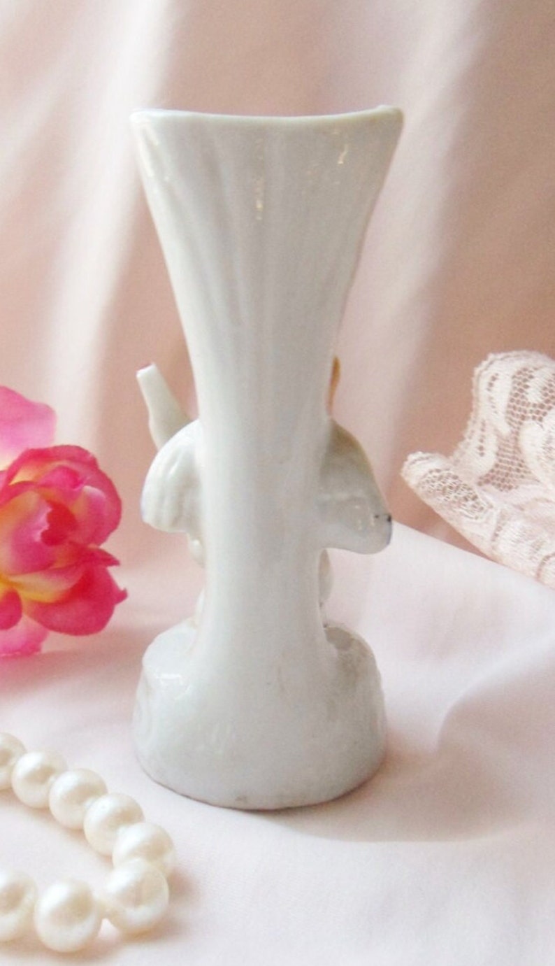 May include: White porcelain vase with a floral design. The vase is shaped like a trumpet and has a flared opening. The floral design is in shades of pink and yellow.